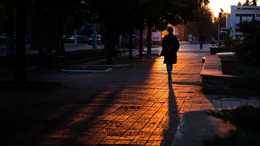 Silhouette einer Person bei Sonnenuntergang auf einem städtischen Weg, umgeben von warmem, goldenem Licht und langen Schatten.