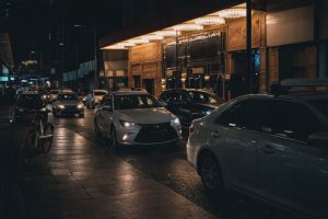 Autos bei Nacht unter warmen Lichtern eines Gebäudes.