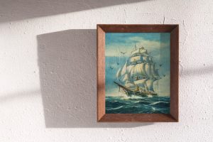 Ein gerahmter Kunstdruck eines Segelschiffs an einer hellen Wand mit Schatteneinfall.