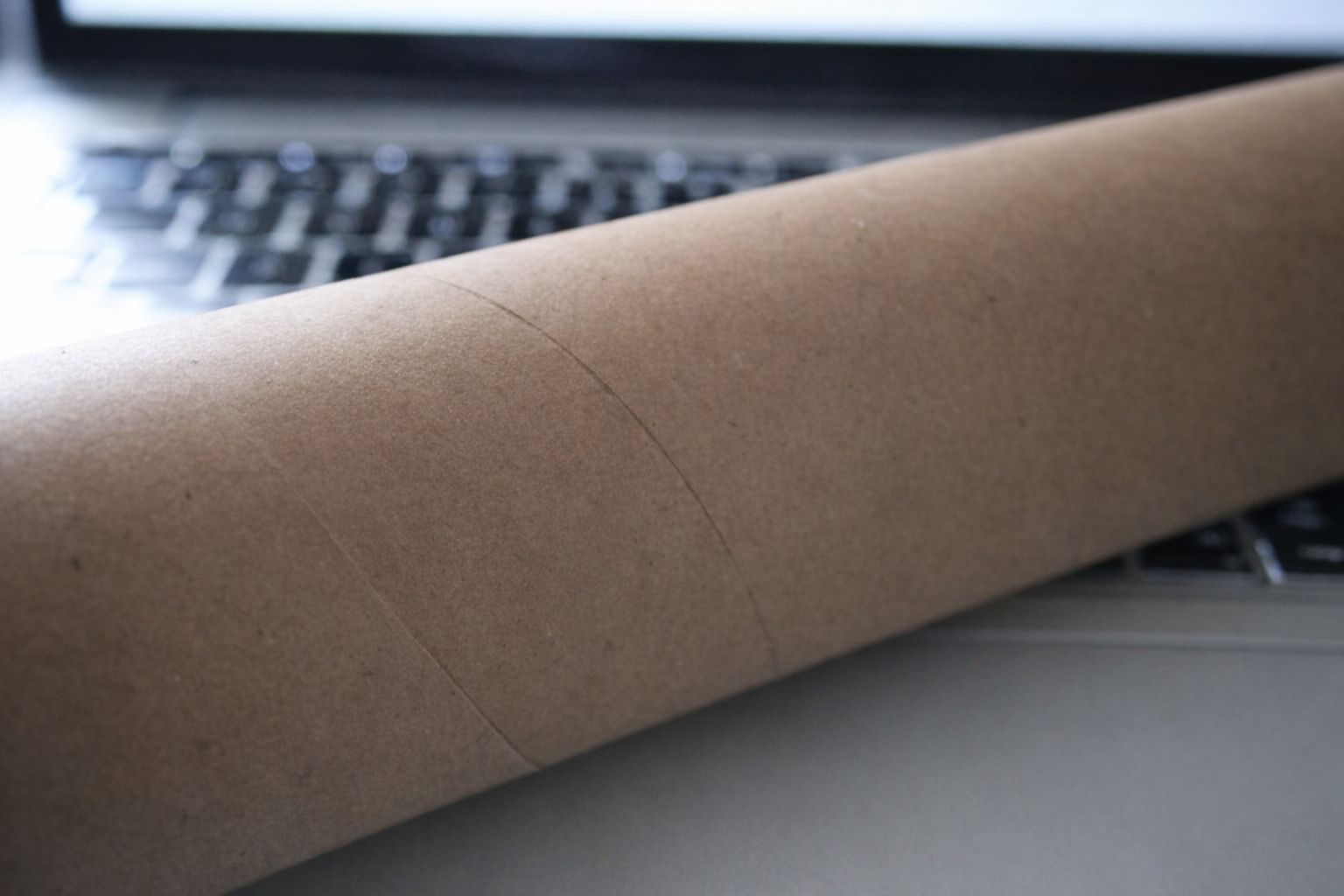 Braune Versandrolle aus Pappe vor einem Laptop für den Fotoversand.